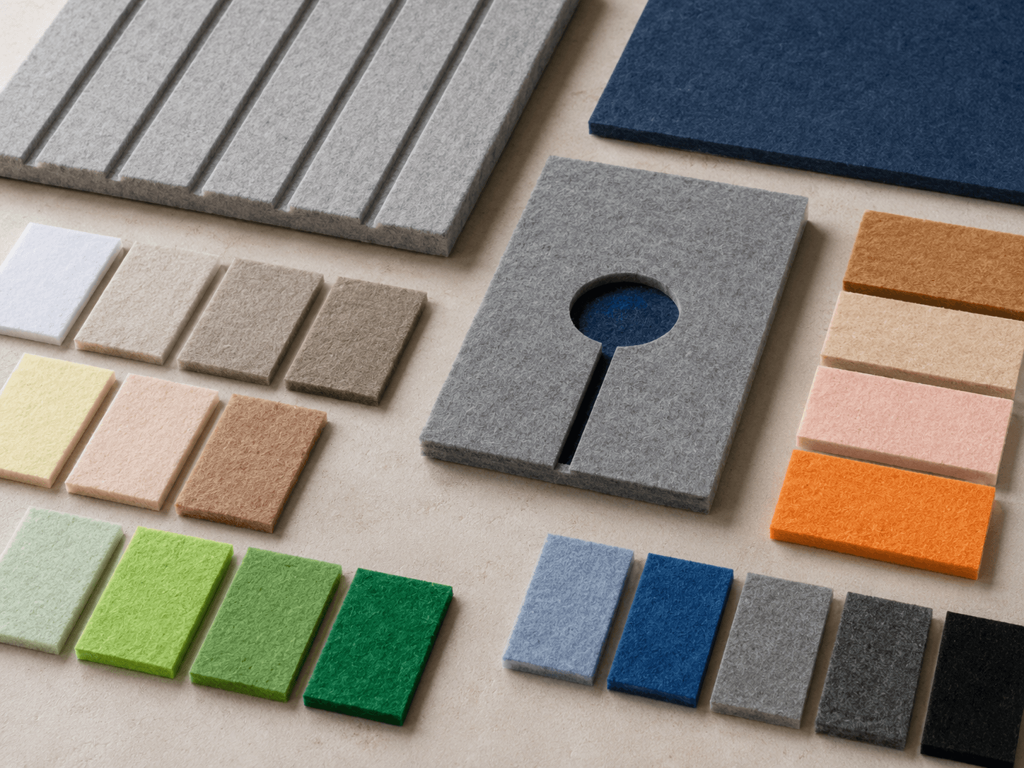 Tabletop arrangement of flat PET acoustic panel samples in multiple colors, including a grooved panel and a CNC-cut panel.